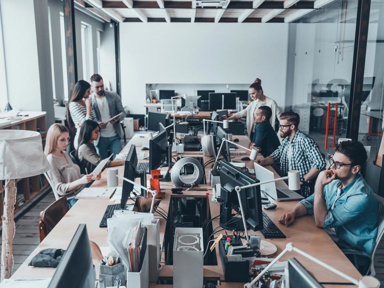 A group of people working in an open office, everyone sitting at their desk, working in the creative industries